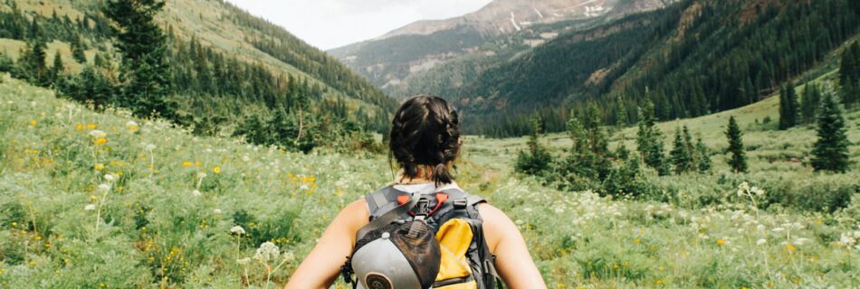 person carrying yellow and black backpack walking between green plants